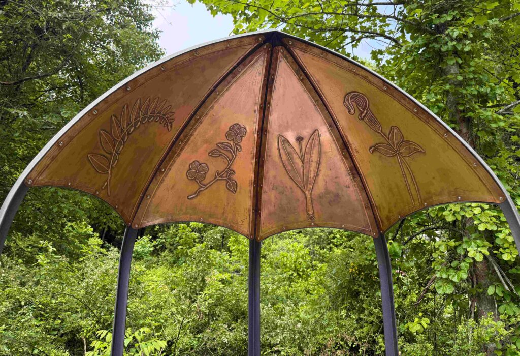 a metal-framed sculpture with four copper panels with a different forest plant embossed in each panel: Solomon's seal, flowering dogwood, ramps, and Jack-in-the-pulpit.